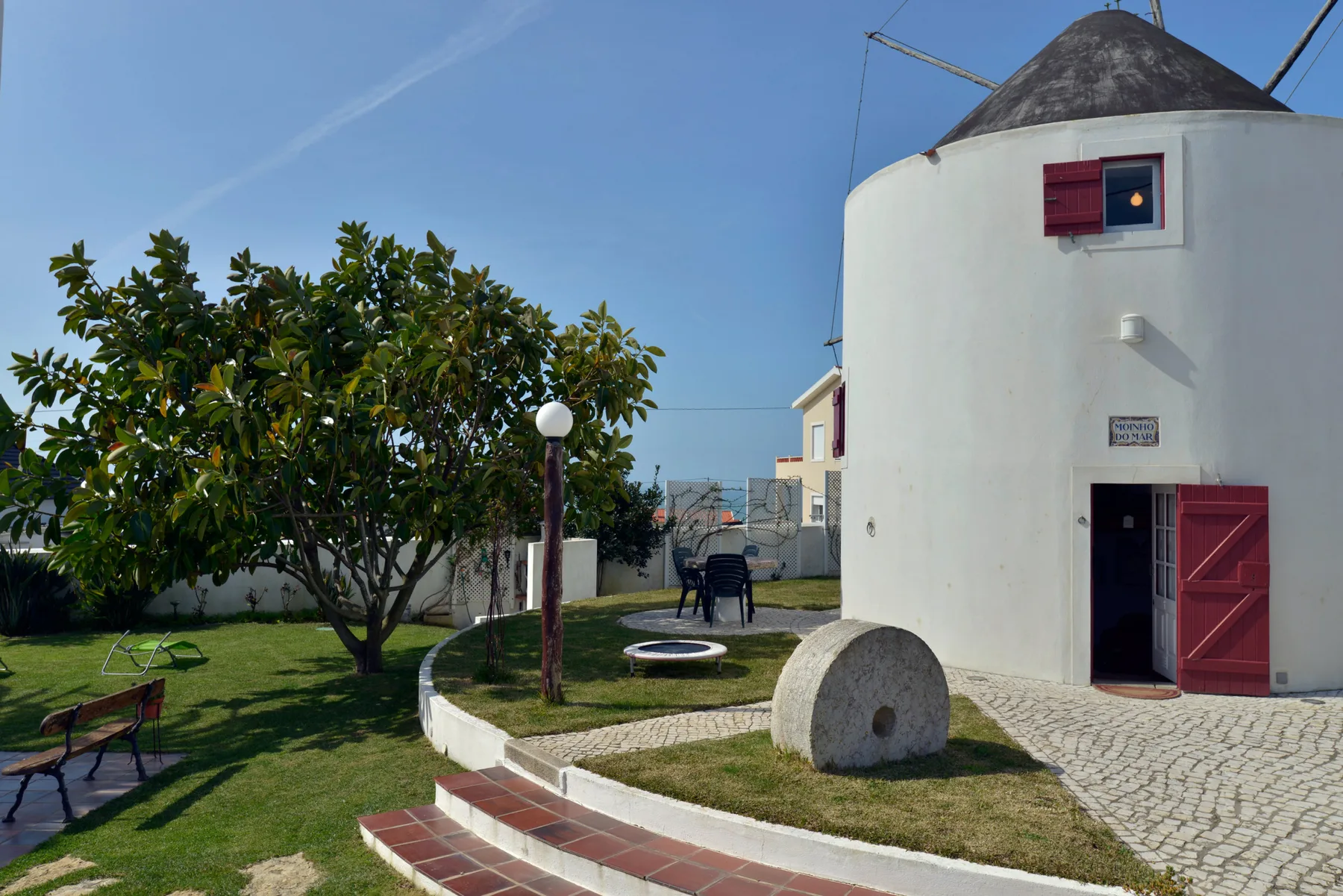 Un molino blanco se alza junto a un jardín y un camino pavimentado.