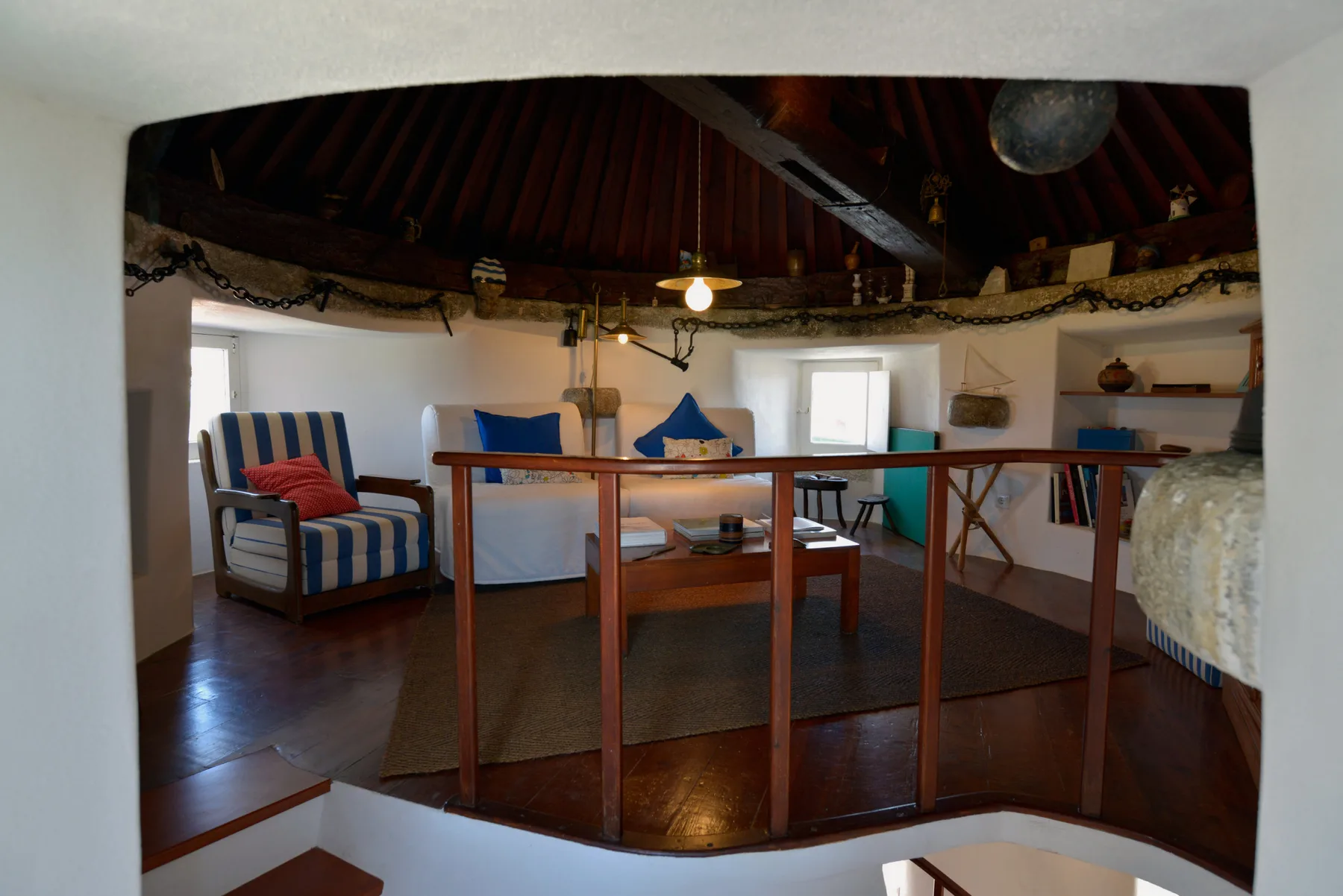 Una sala de estar redonda tiene asientos a rayas, una mesa central y un techo de madera oscura.