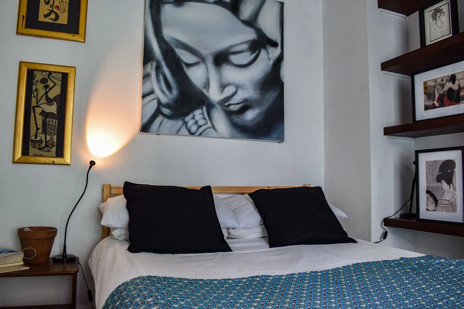 Un dormitorio con una cama, almohadas oscuras y cuadros en las paredes.