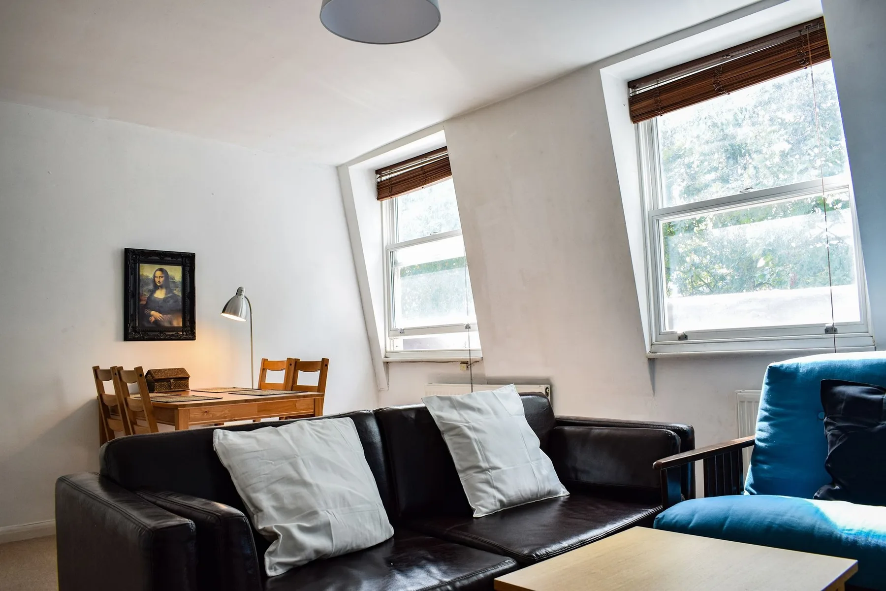 Una sala de estar con asientos oscuros, dos ventanas y una pequeña mesa de comedor.