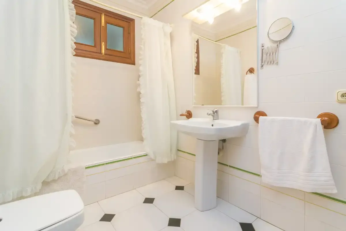Un baño luminoso con lavabo de pedestal, bañera y azulejos blancos.