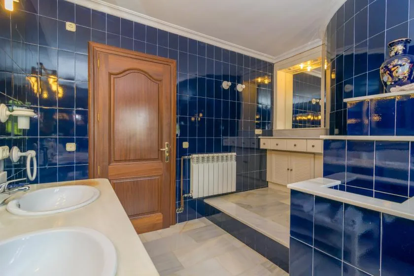 Un baño alicatado con una puerta de madera, un tocador y dos lavabos.