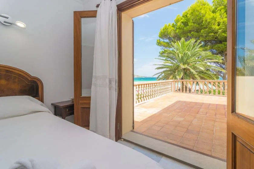 Un dormitorio da a una terraza soleada con vistas a palmeras y al mar.