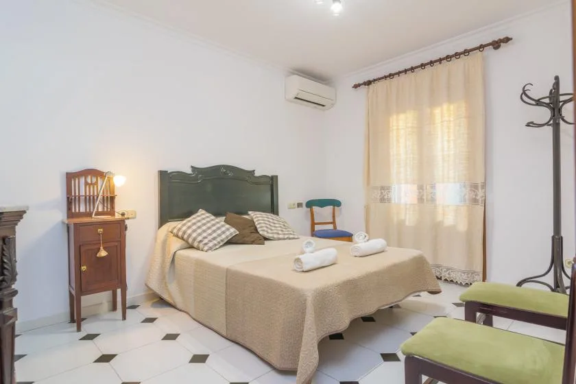 Un dormitorio con una cama tendida, una mesita de noche y una ventana con cortinas.