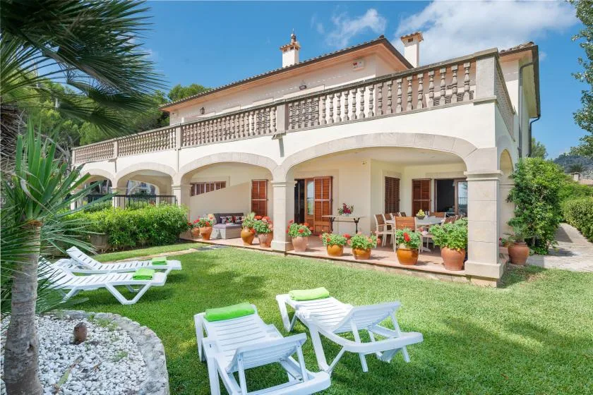 A two-story house with a covered patio opens onto a lawn with lounge chairs.