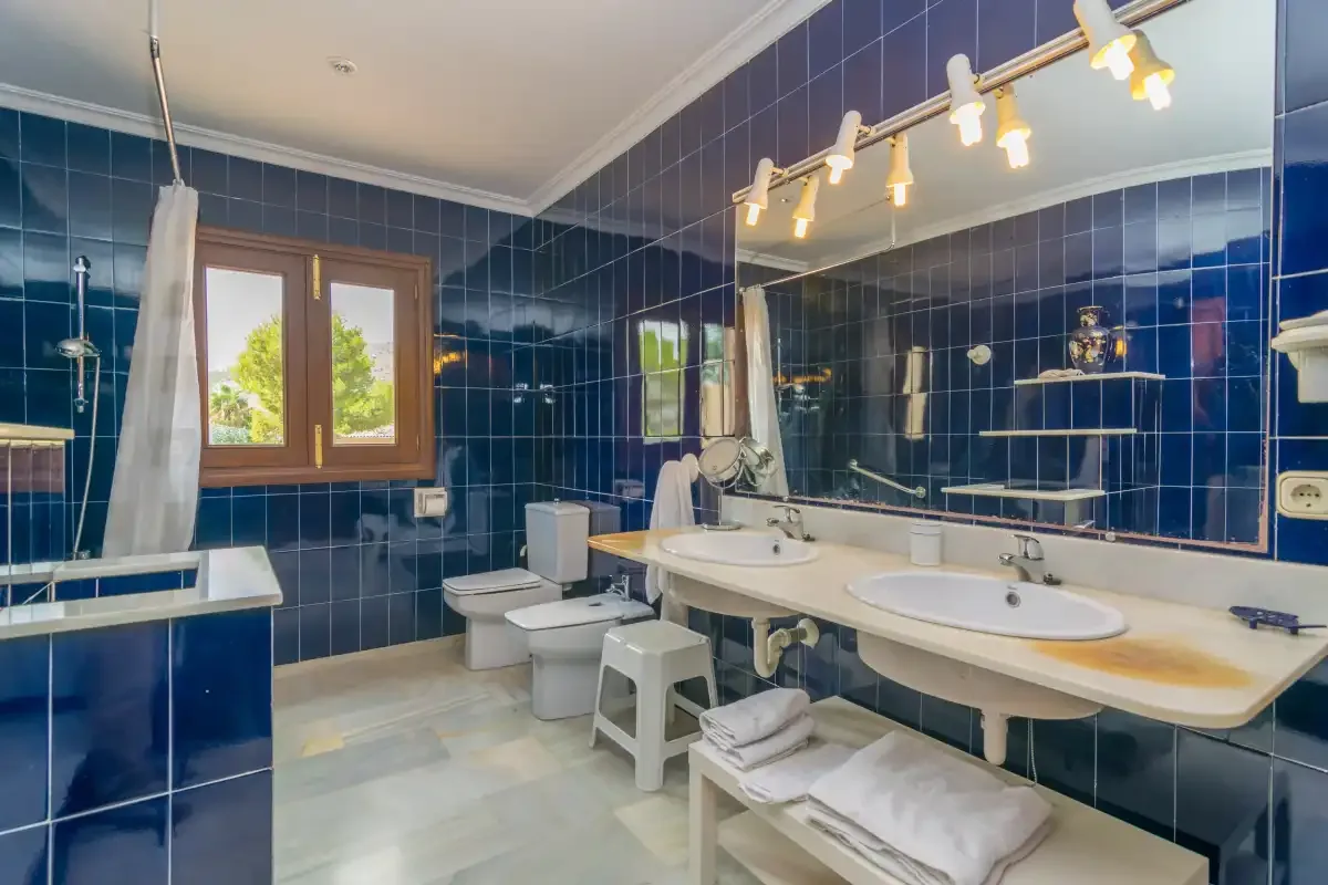 Un baño con paredes de azulejos azules, una bañera y un lavabo doble.