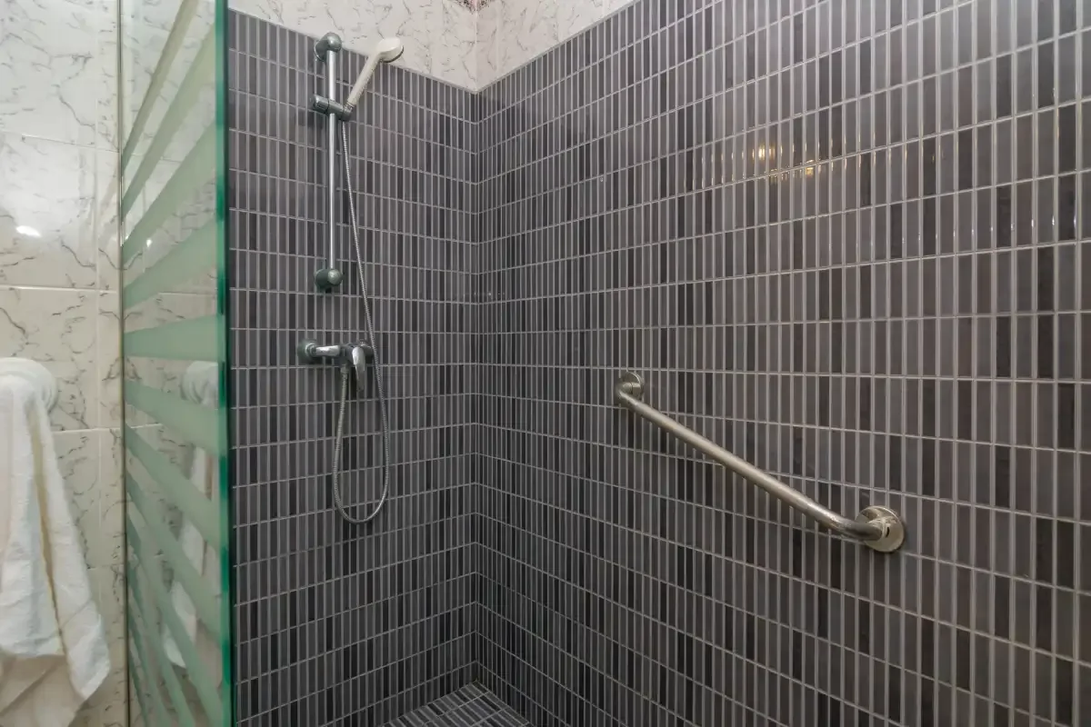 Una zona de ducha alicatada con una ducha de mano y una barra de apoyo en la pared.