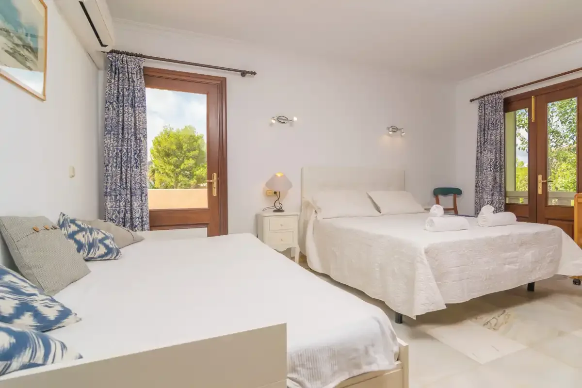 Un dormitorio luminoso con dos camas, mesillas de noche y grandes ventanas.