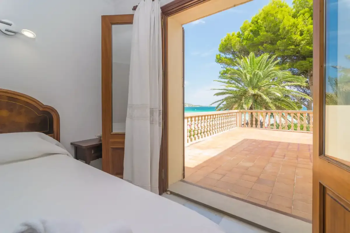 Un dormitorio da a una terraza de baldosas con palmeras y vistas al mar.