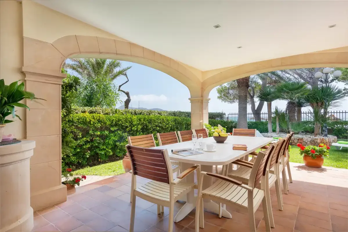 Una zona de comedor exterior cubierta se abre a un jardín.