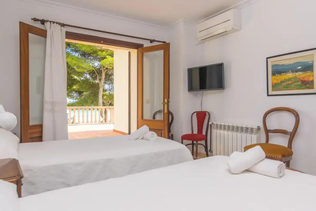 Un dormitorio luminoso con ropa de cama blanca y la puerta del balcón abierta.