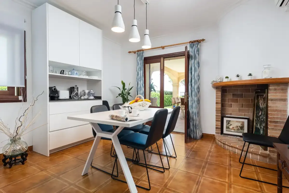 Un comedor luminoso con una mesa junto a una chimenea de ladrillo y puertas de cristal.