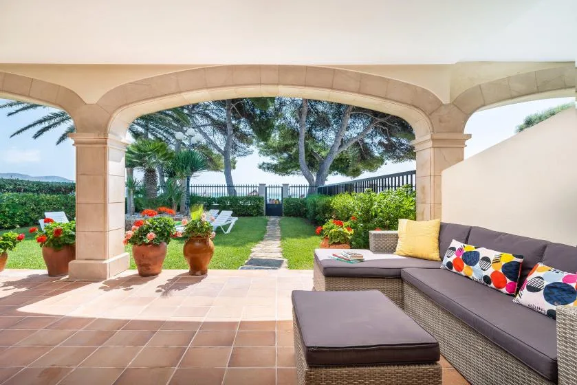 Un patio cubierto con asientos al aire libre da a un jardín y al mar.