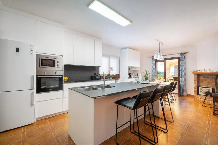 Una cocina luminosa con una isla y taburetes se abre a un comedor.