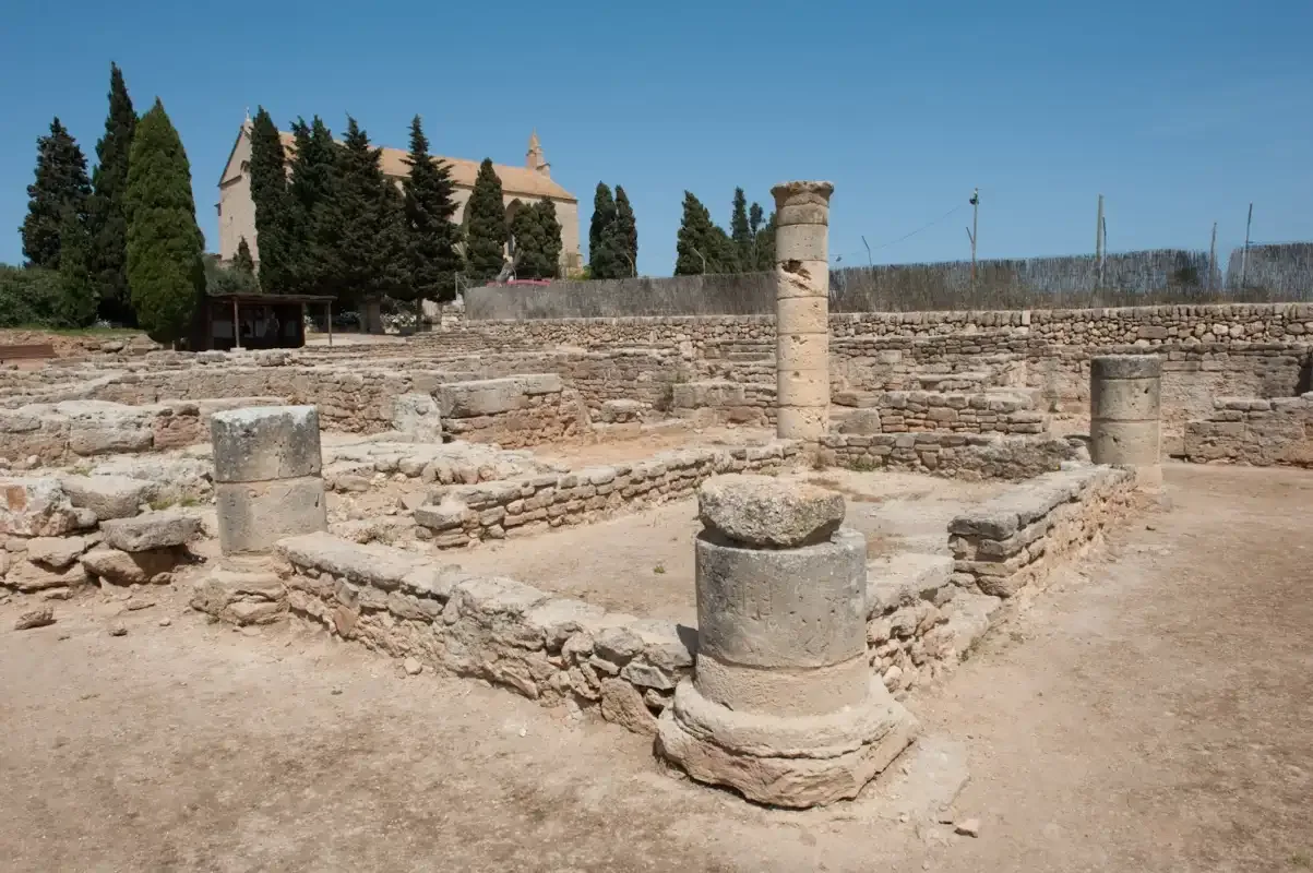 Ruinas antiguas de piedra con muros bajos y restos de columnas bajo un cielo despejado.
