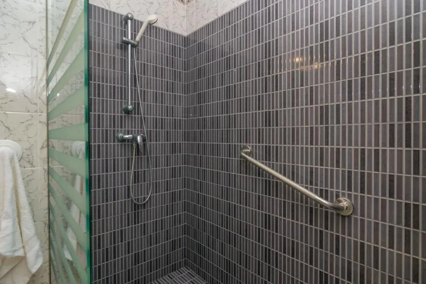 Una zona de ducha con azulejos, una barra de apoyo y una ducha de mano.
