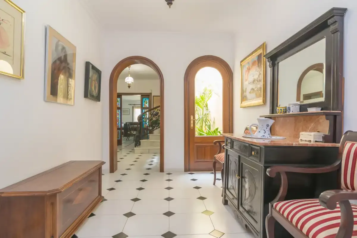 Un pasillo interior con puertas arqueadas, cuadros en las paredes y suelo de baldosas.