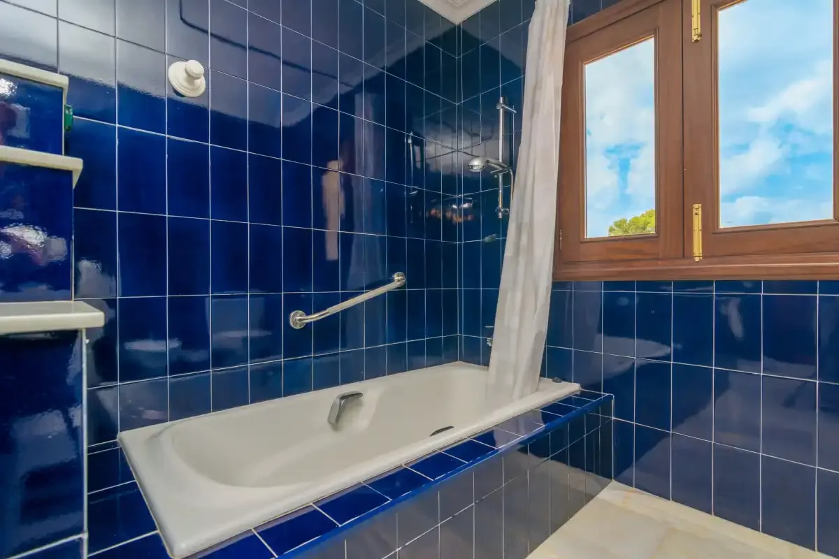 Un baño con bañera, paredes alicatadas y una ventana.