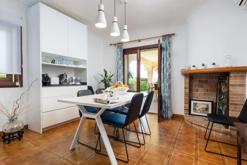 Comedor con una mesa blanca y asientos oscuros junto a una chimenea de ladrillo.