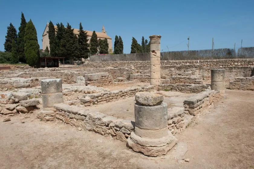 Un yacimiento arqueológico con muros bajos de piedra y restos de columnas.