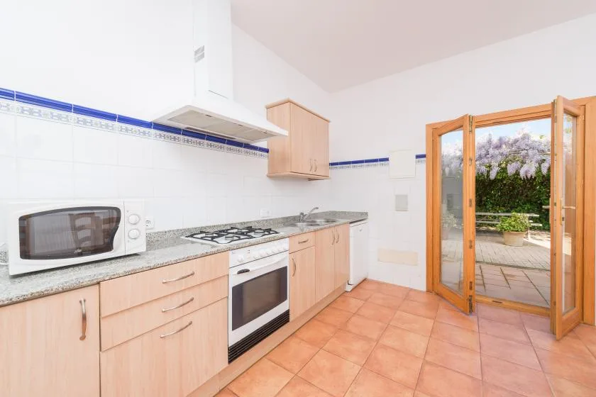 A bright kitchen with wood cabinets, a countertop, and an open patio door.