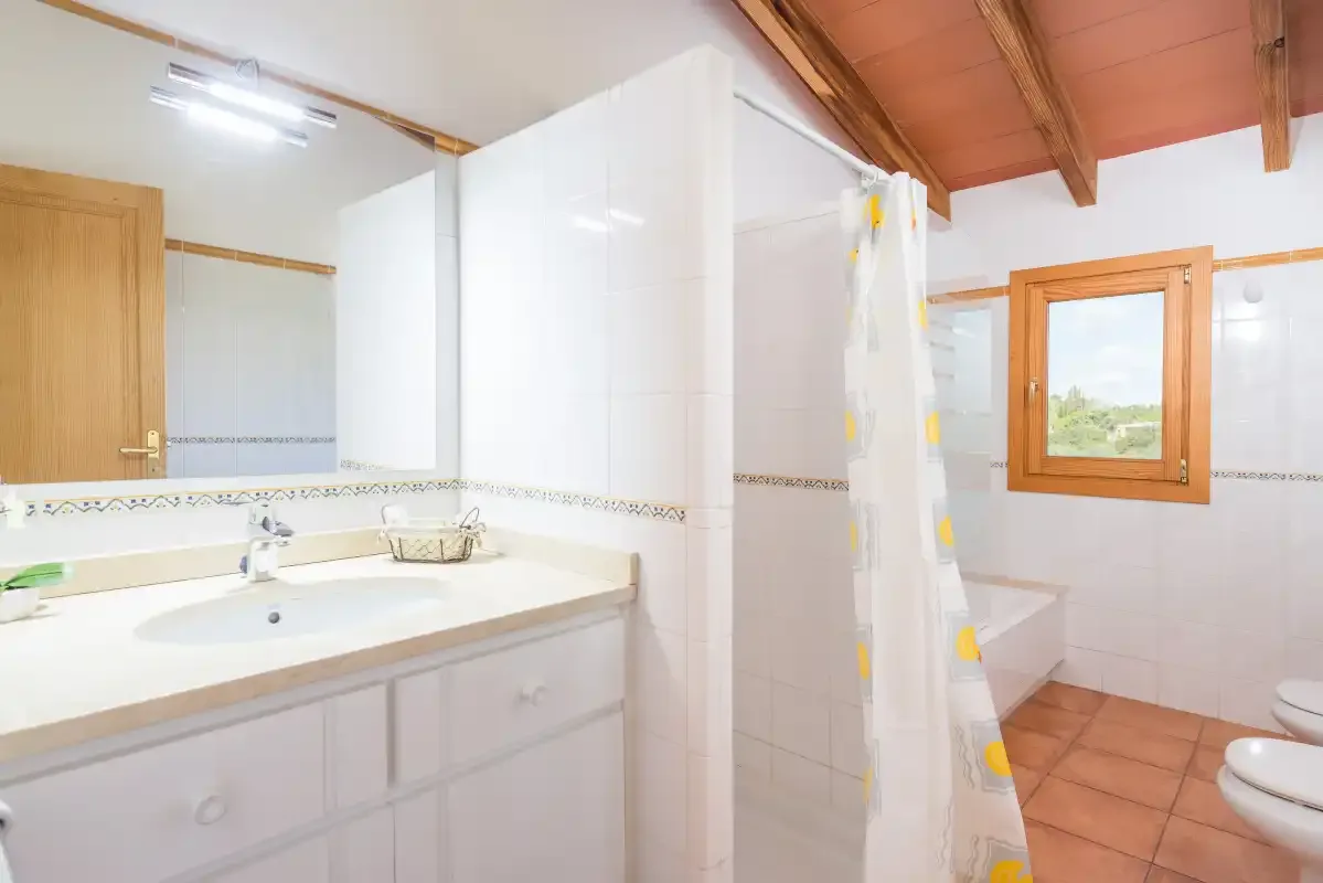 A tiled bathroom with a sink, shower curtain, and window.