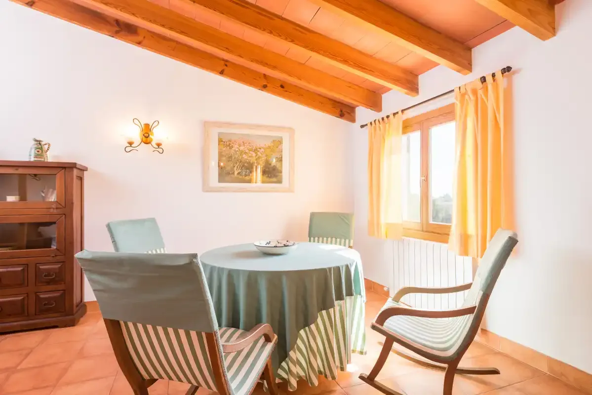 A dining area with a round table and seating beneath exposed wooden ceiling beams.
