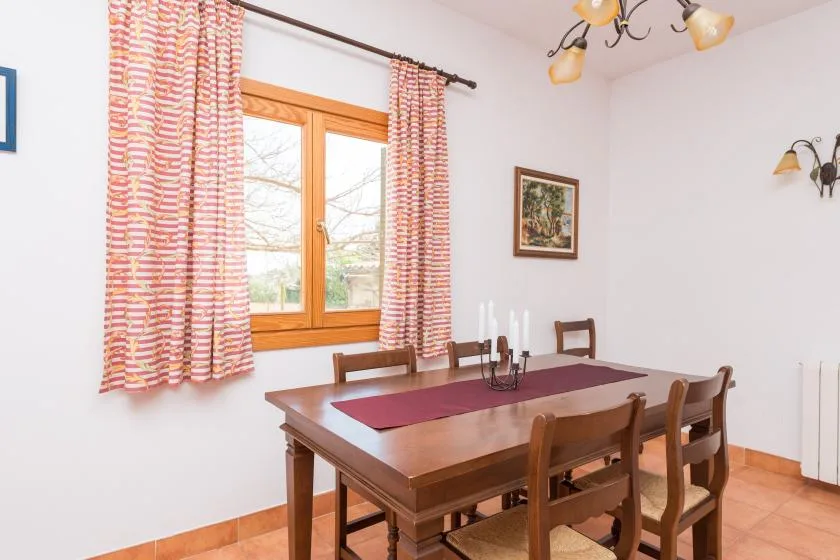 A dining room with a wooden table set beneath a window with patterned curtains.