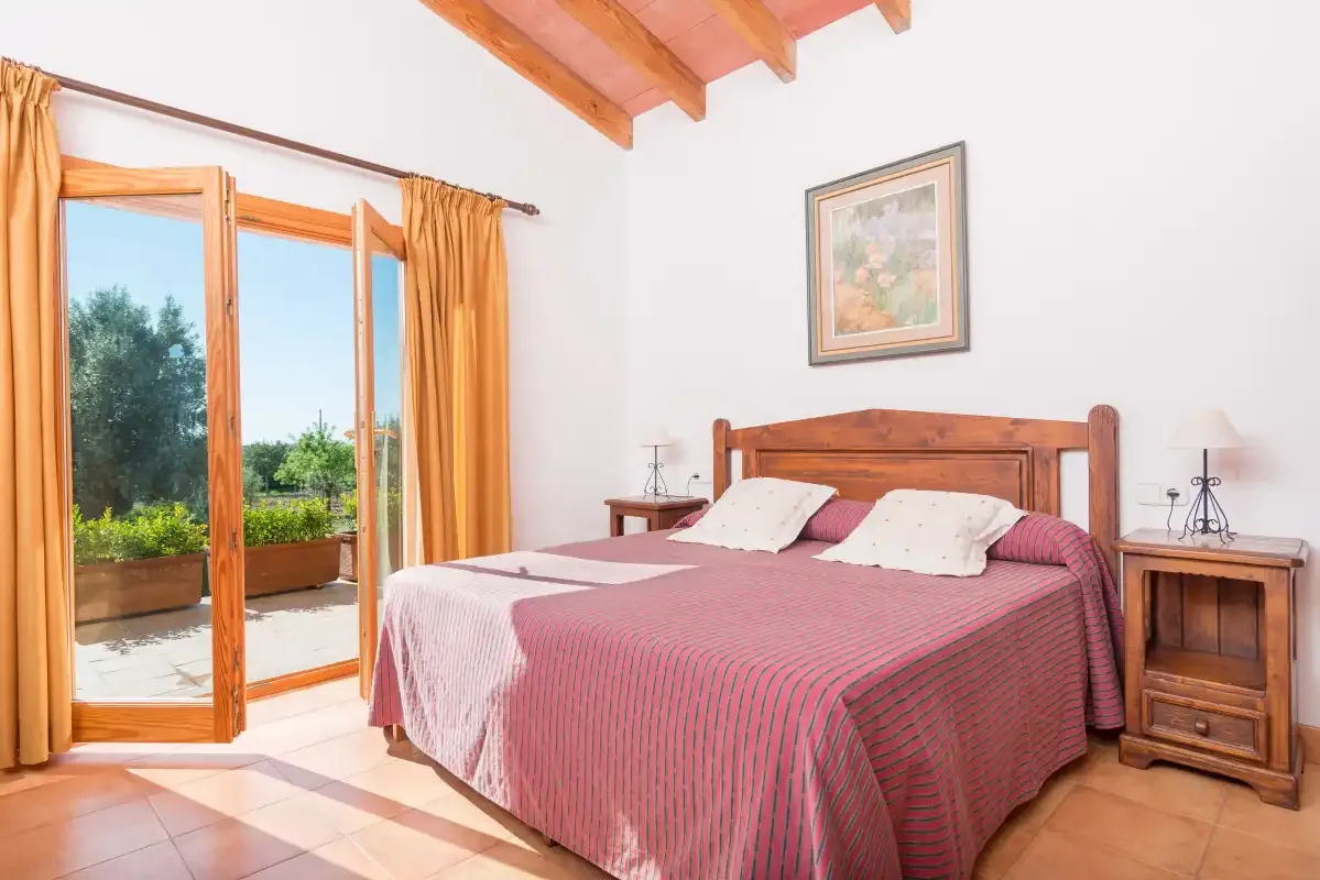 A bedroom with a double bed, wooden bedside tables, and open doors to a patio.