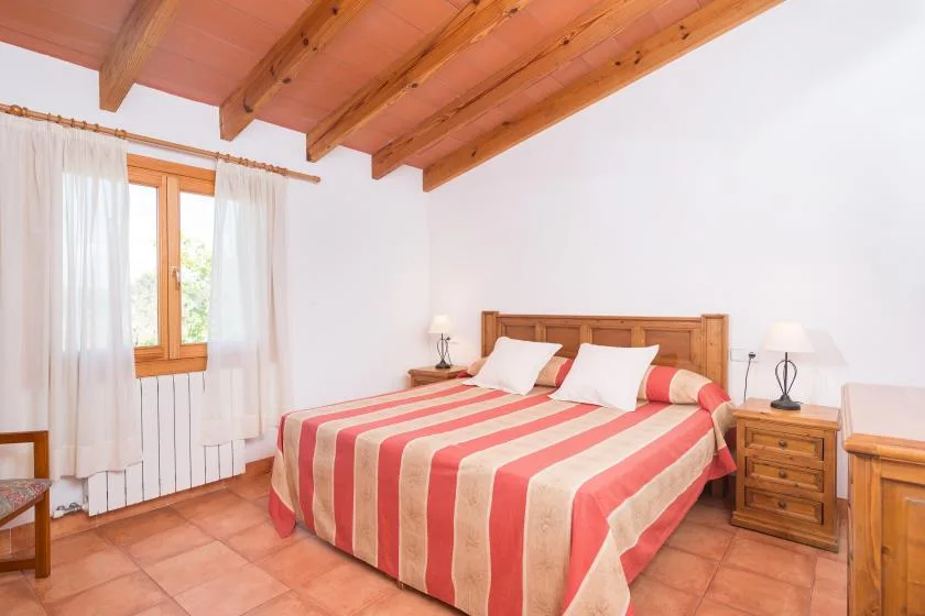 A bedroom with a double bed, striped bedding, and a wooden ceiling.