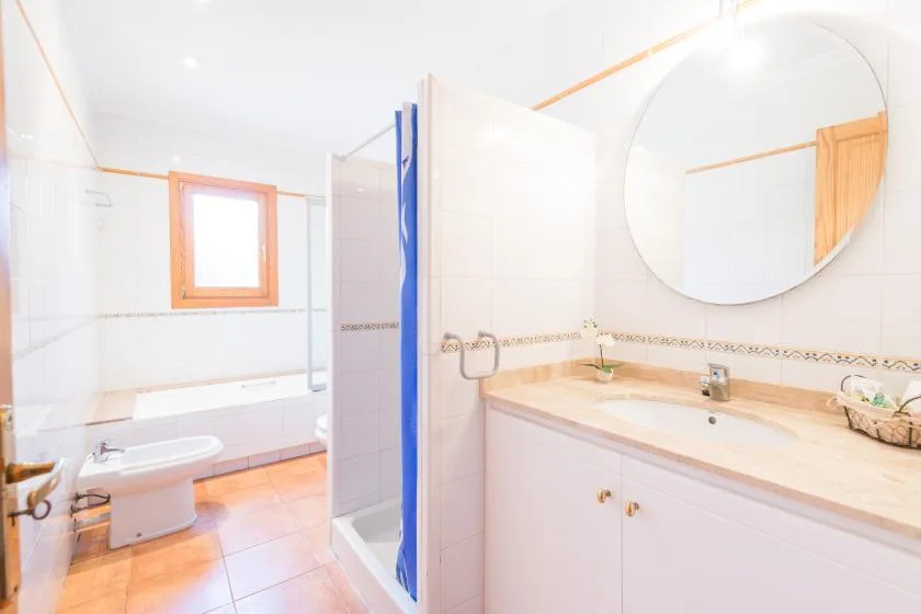 A bright bathroom with a long vanity and a large round mirror.