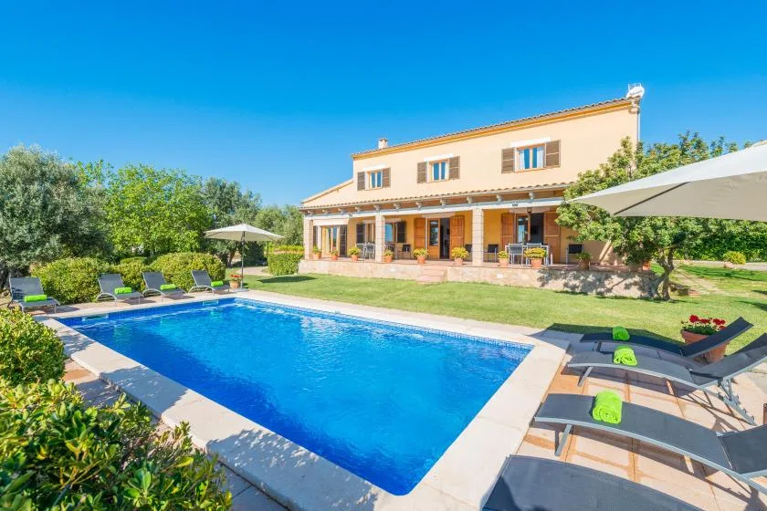 A villa and garden patio overlook a rectangular swimming pool.