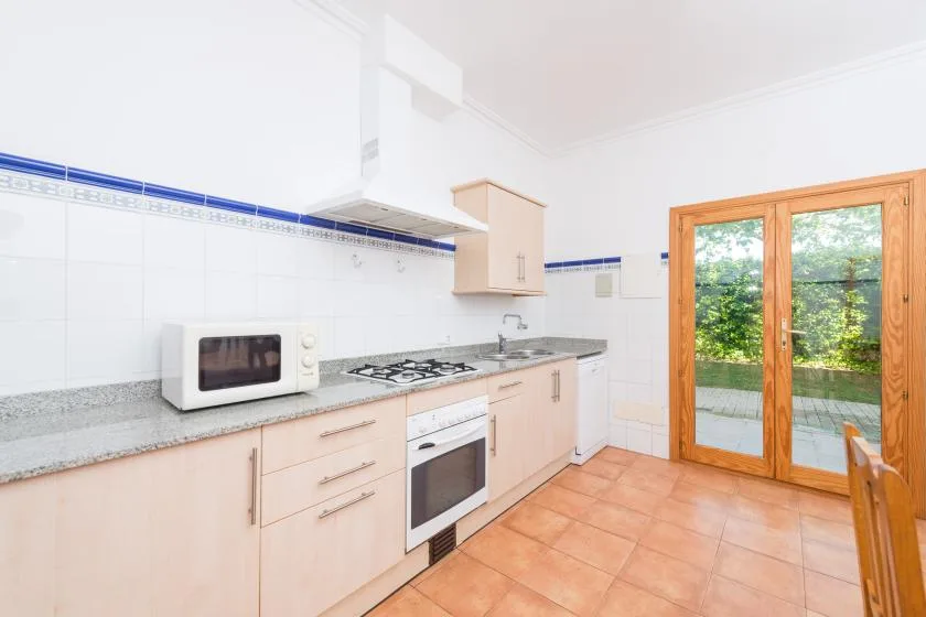 A bright kitchen with a countertop, cooking range, and glass doors opening onto greenery.