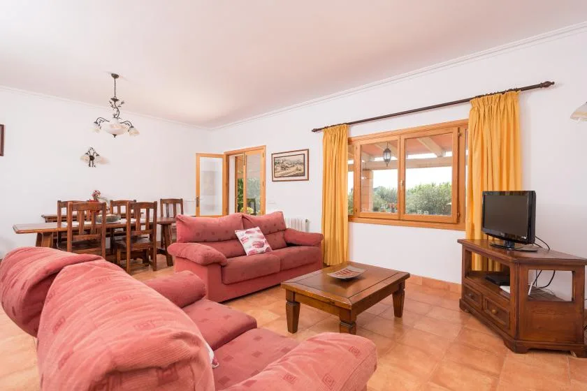 A living room with pink seating, a wooden coffee table, and a dining area by the window.