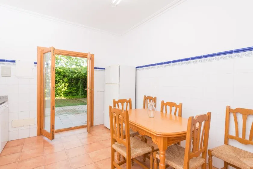 A dining room with a wooden table and chairs beside an open garden-facing doorway.