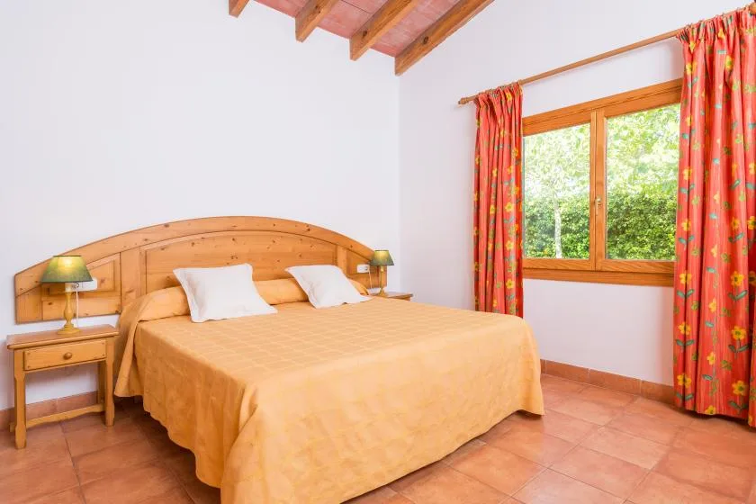A bedroom with a double bed, bedside tables, and a window with red curtains.
