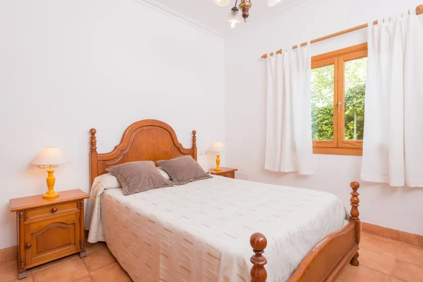 A bedroom with a wooden bed and a window framed by white curtains.