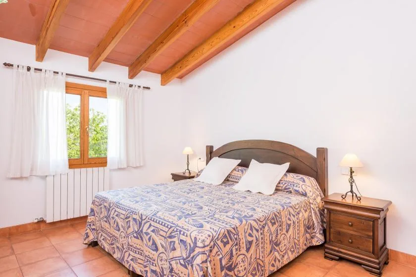 A bedroom with a double bed, bedside tables, and a window with curtains.