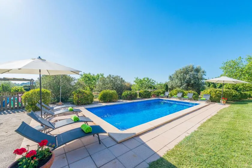 An outdoor swimming pool is surrounded by lounge seating, umbrellas, and greenery.