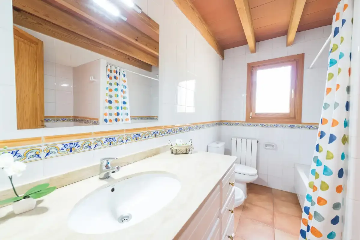 A tiled bathroom with a sink, toilet, and colorful shower curtain.