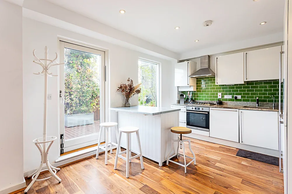A bright kitchen with a breakfast island, green tile backsplash, and glass patio doors.