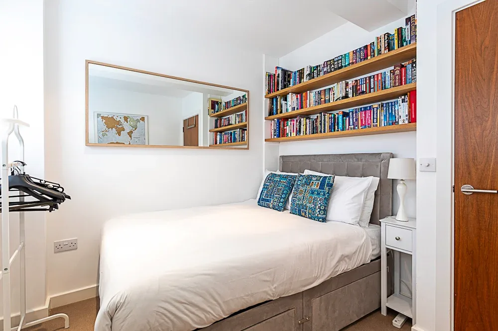 Un dormitorio con una cama tendida bajo estantes de libros en la pared.