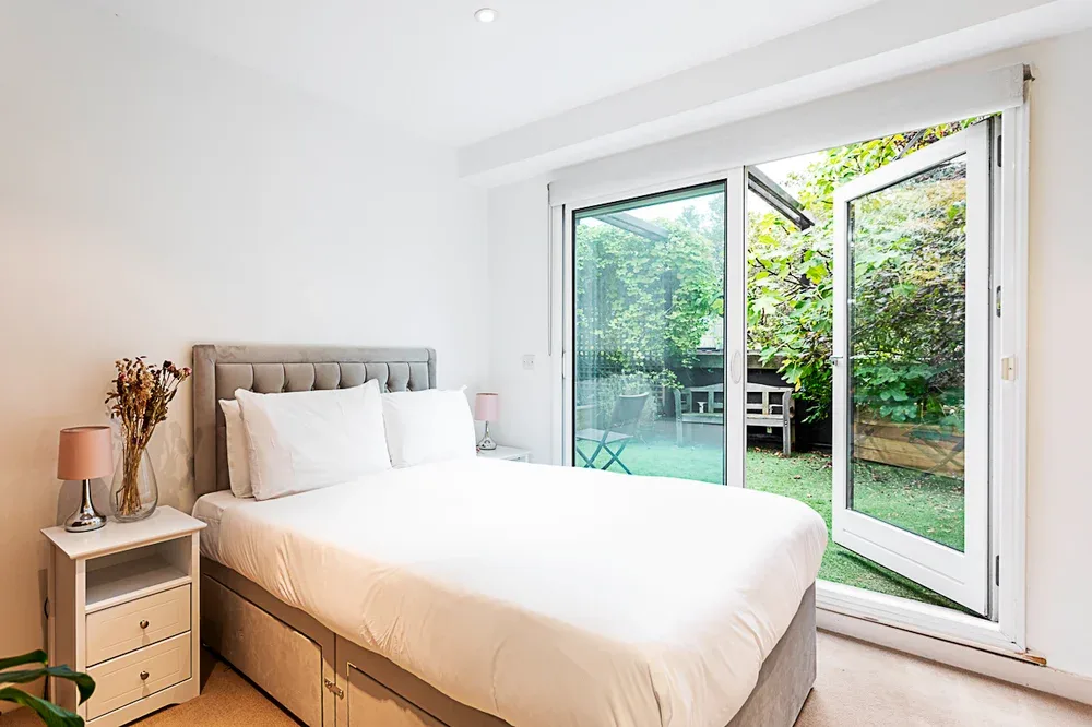 A bright bedroom with a large bed beside glass doors opening onto a garden.
