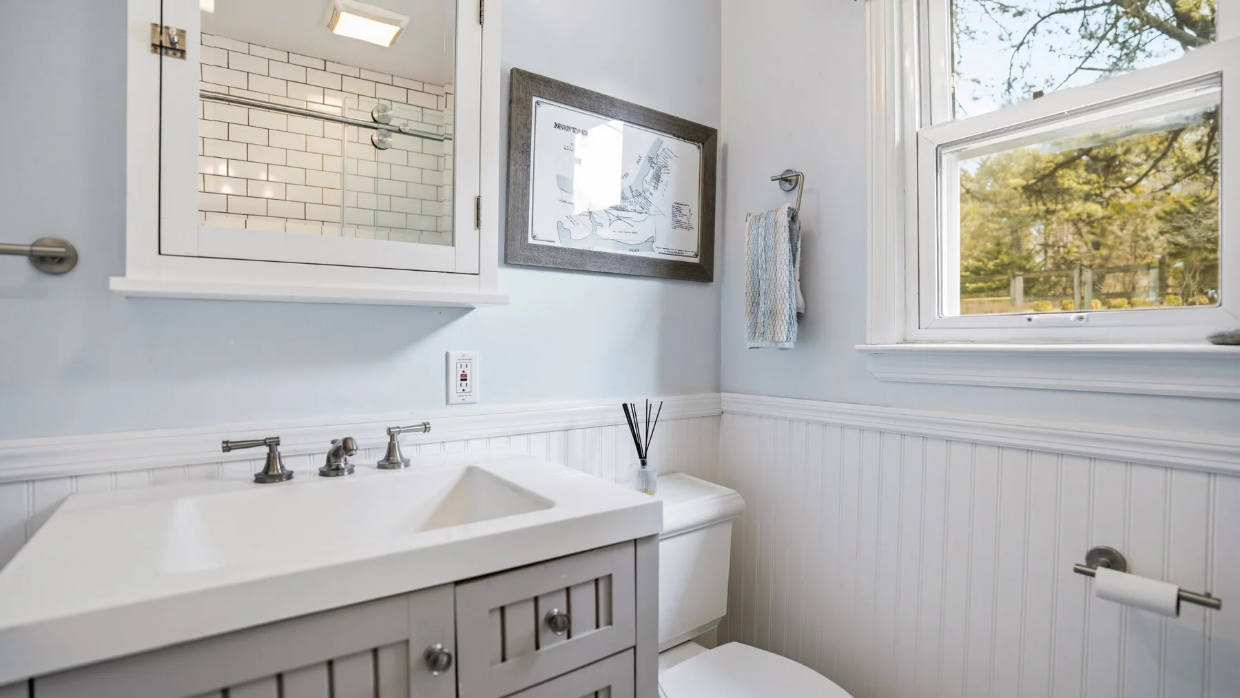 Un baño luminoso con lavabo, inodoro y una ventana con vista a los árboles.