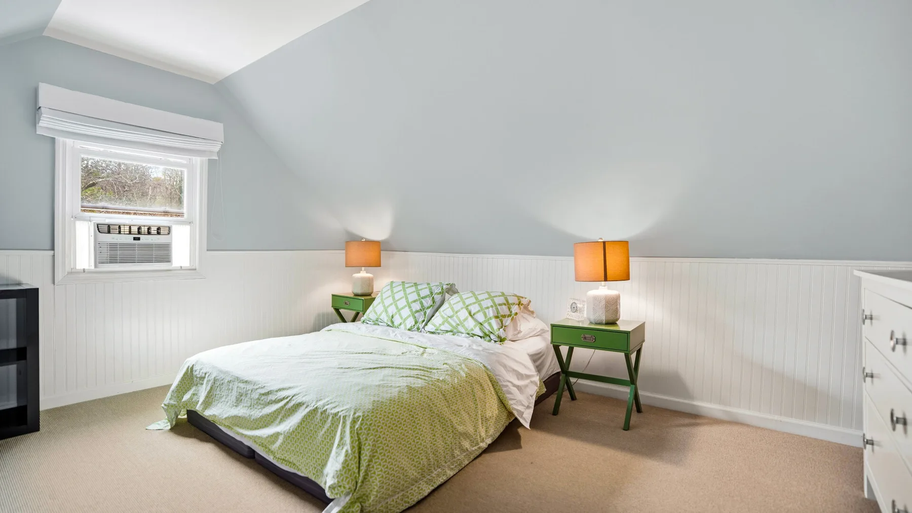 Un dormitorio con una cama, ropa de cama verde y mesitas de noche.
