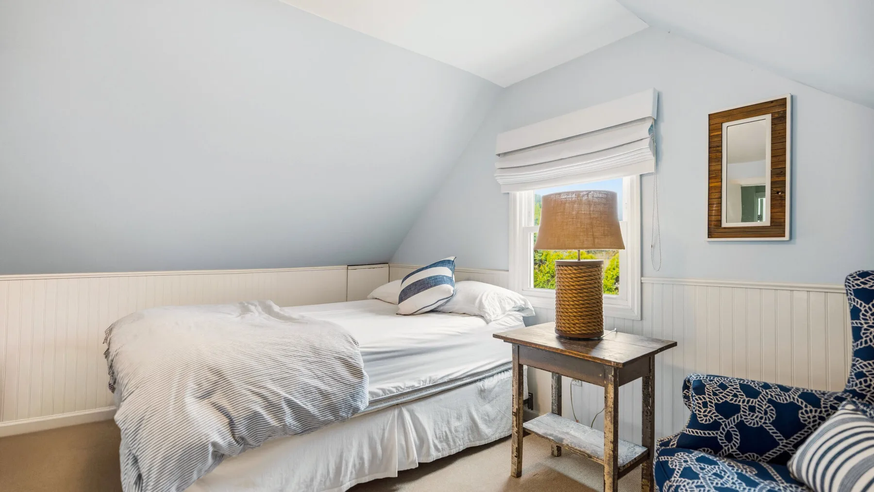 Un dormitorio luminoso con una cama junto a una ventana y una mesita.