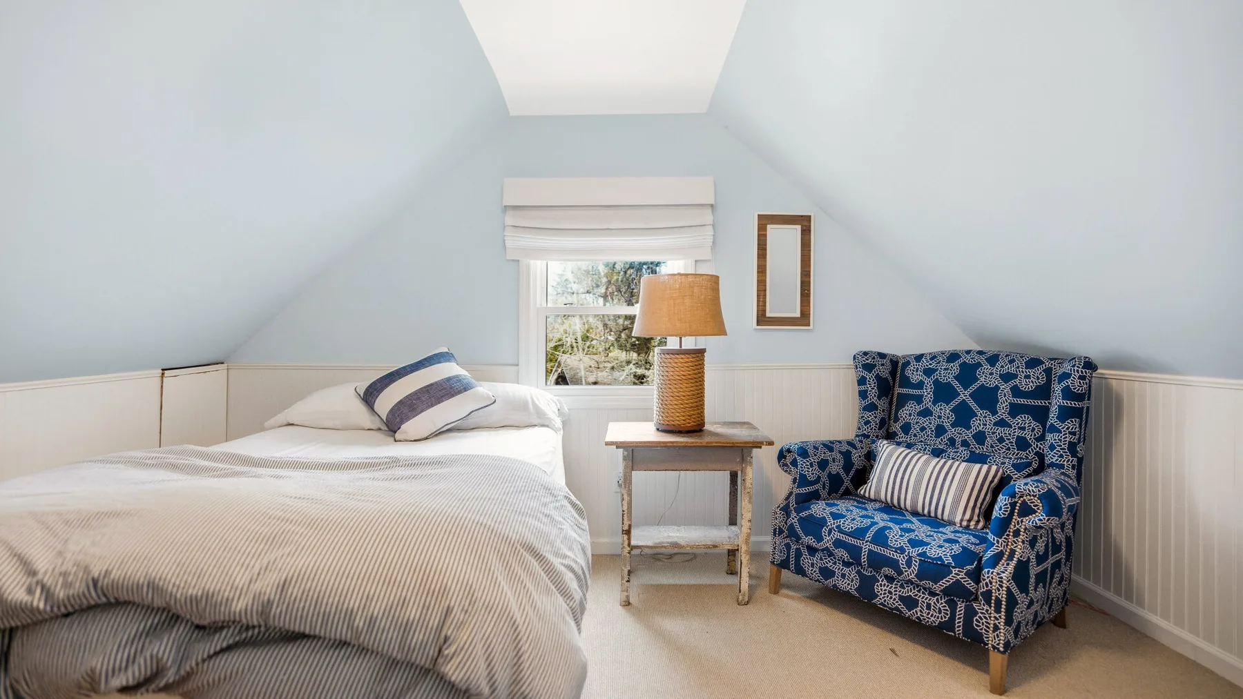 Un dormitorio luminoso con una cama y un sillón estampado bajo un techo inclinado.