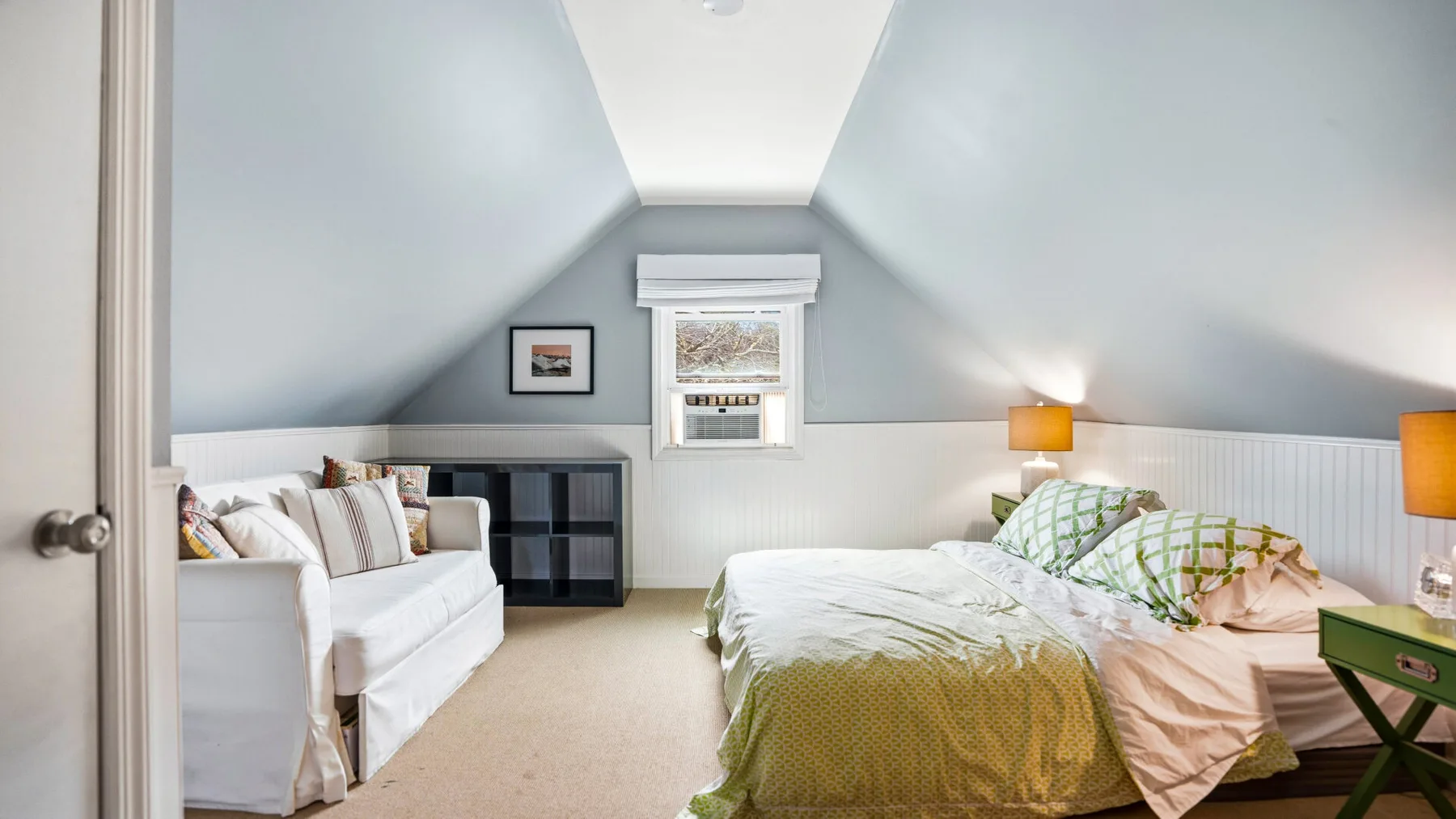 Un dormitorio luminoso bajo el techo inclinado, con una cama y una ventana pequeña.