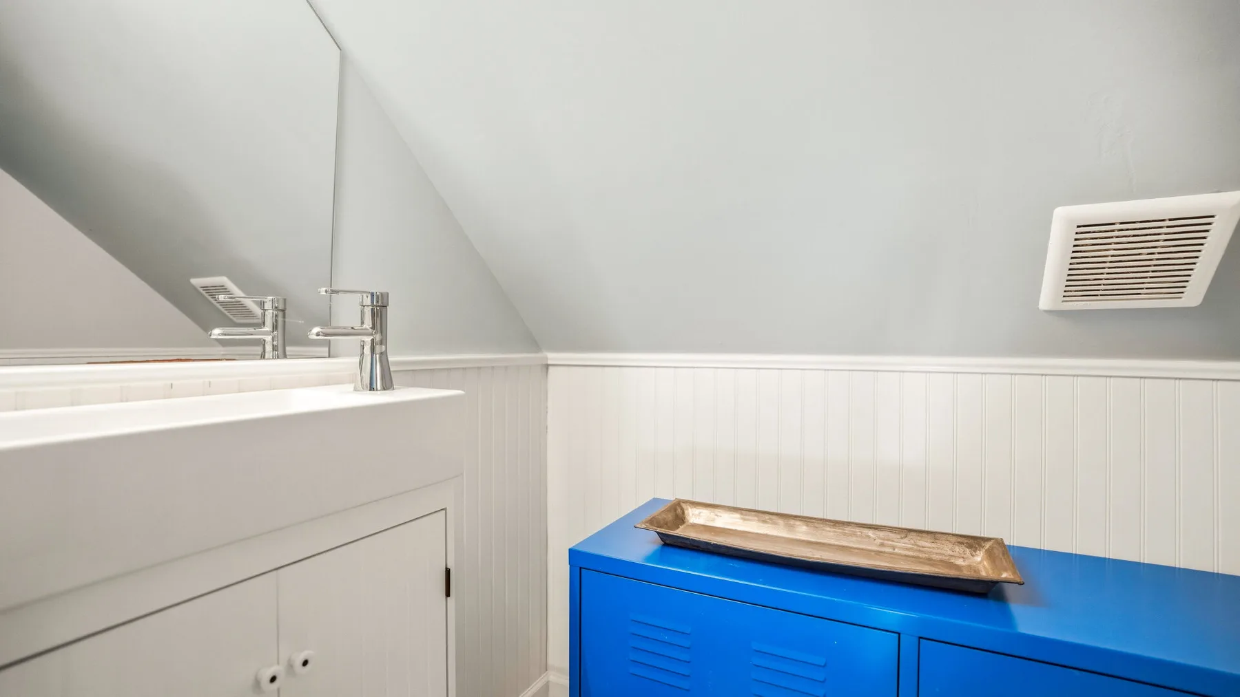 Un baño luminoso con un mueble blanco y un armario azul bajo el techo inclinado.