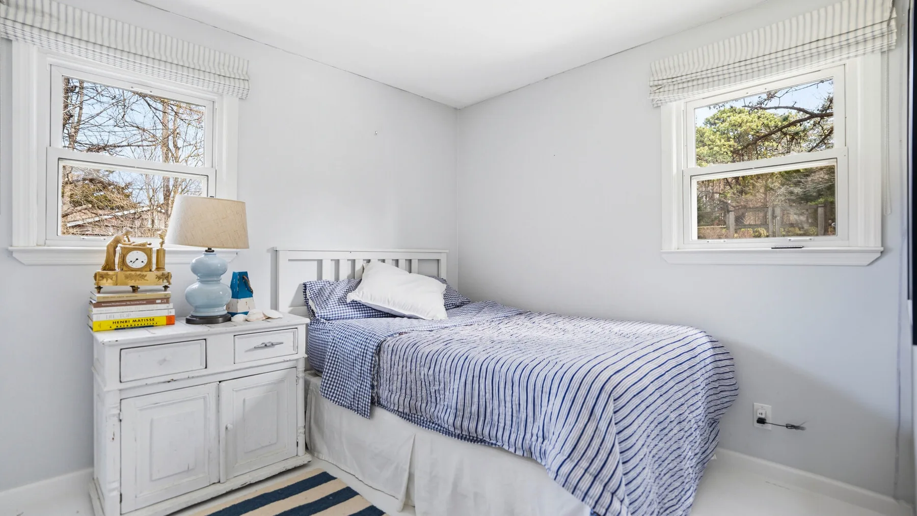 Un dormitorio luminoso con una cama vestida con ropa de cama a rayas azules y blancas.